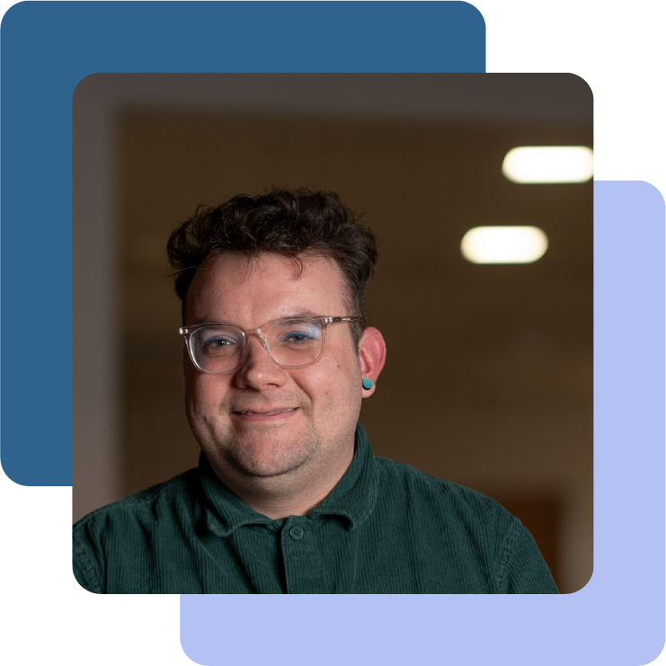 Connor is a young white non-binary person with short brown curly hair and light facial hair. They are pictured smiling wearing glasses and a green corduroy shirt.