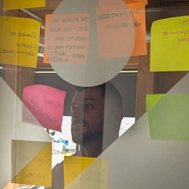 Looking through a frosted glass window with sticky notes affixed to the other side. A man visible through a transparent section is reading their contents.