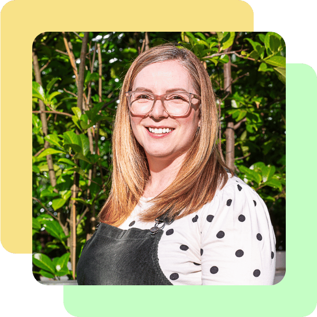 Kim is a middle-aged white woman with wavy brown hair. She's pictured here smiling, wearing glasses, lipstick and her signature black pinafore dress over a white polka dot blouse.