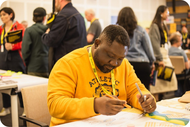 A black student wearing a yellow sweatshirt writing on a service design template with a sharpie.